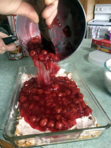 pouring cherry pie filling into cherry pretzel torte