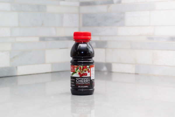 One 8 oz bottle of Montmorency tart cherry concentrate on a white counter with a white tiled backsplash
