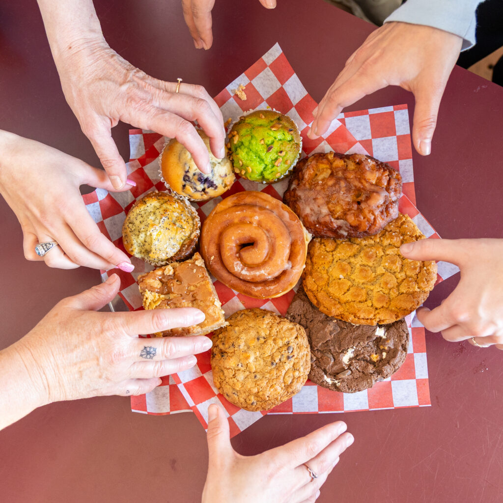 People reaching towards a plate of assorted baked goods