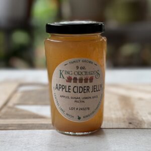 9 oz jar of King Orchards Apple Cider Jelly made from Michigan apples, with simple ingredients—apples, sugar, lemon juice, and pectin—displayed on a rustic wooden surface.